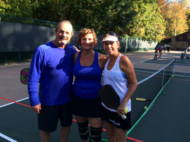 three people standing and smiling in a pickleball court
